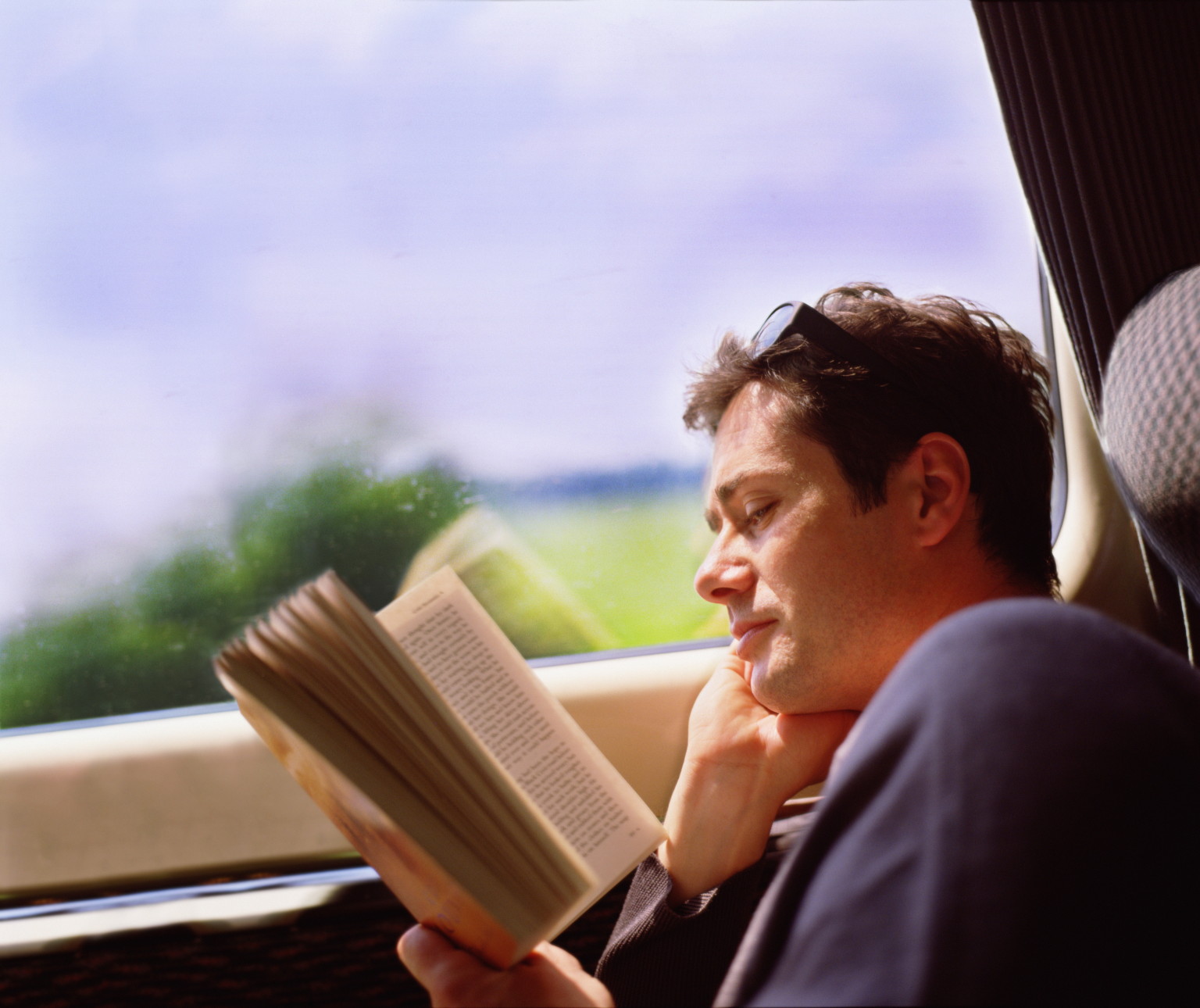 Young man travelling on train, reading book, profile